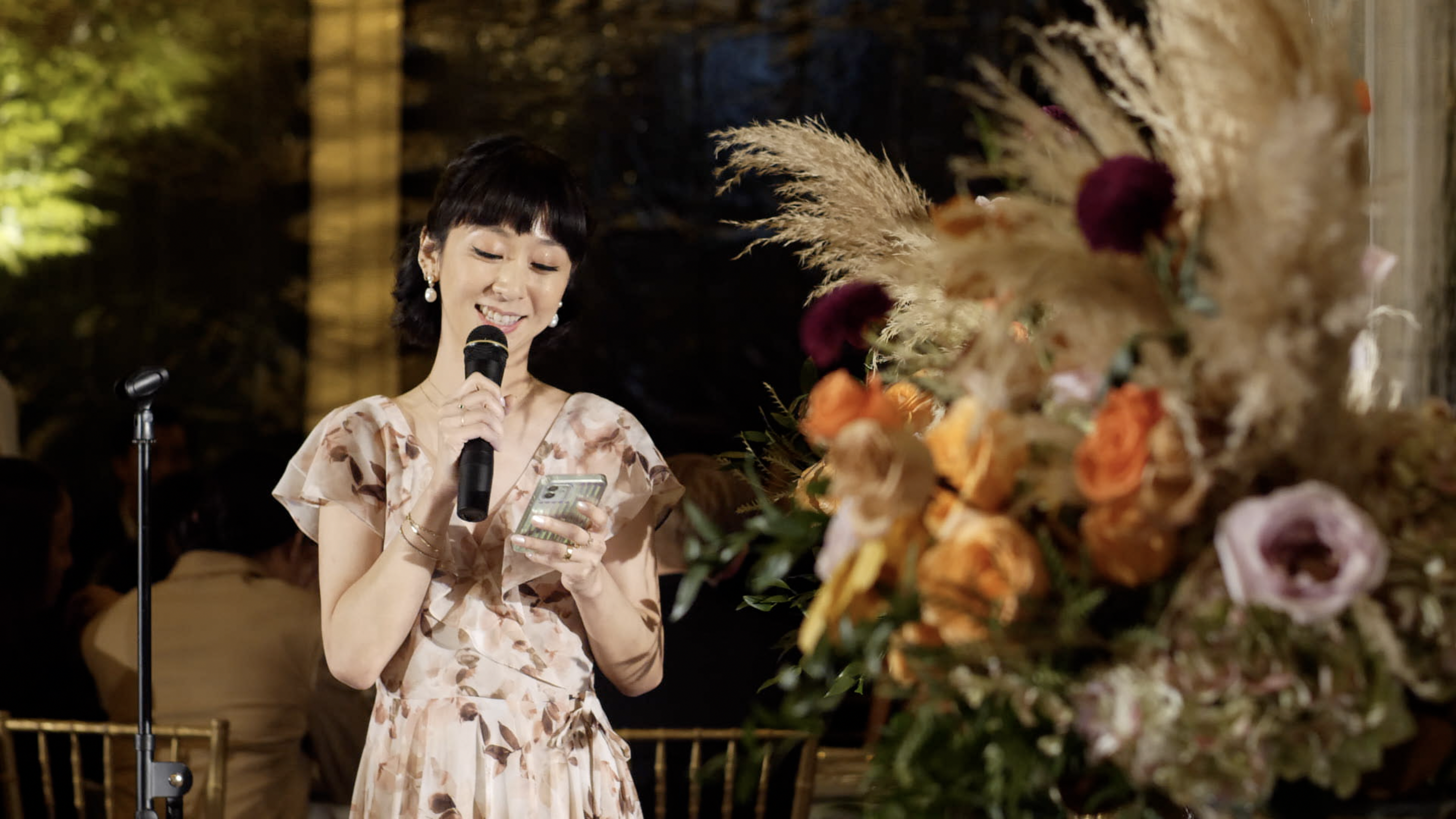 a woman in a floral dress smiles holding a microphone